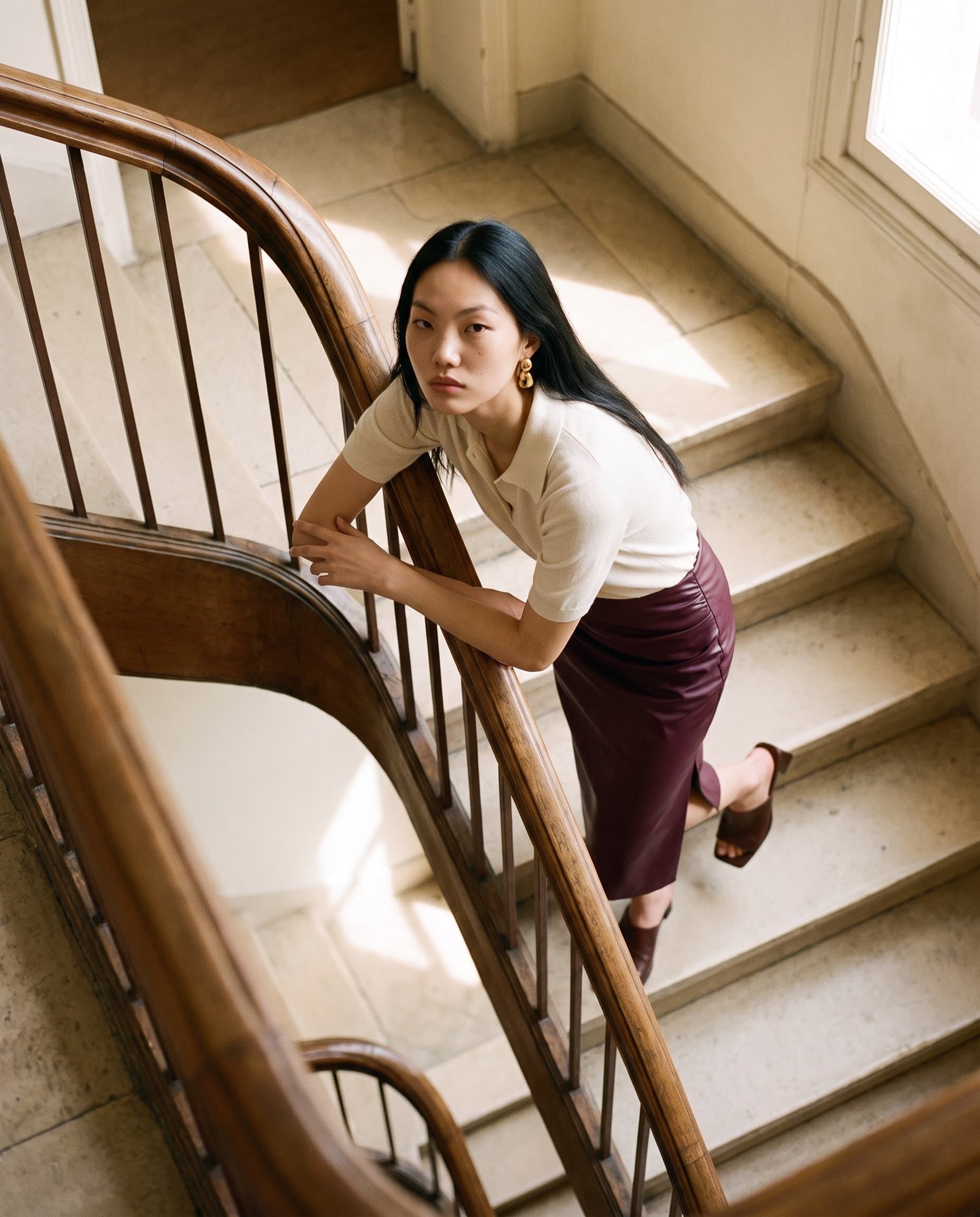 Model leaning on a wooden stair banister, seen from above